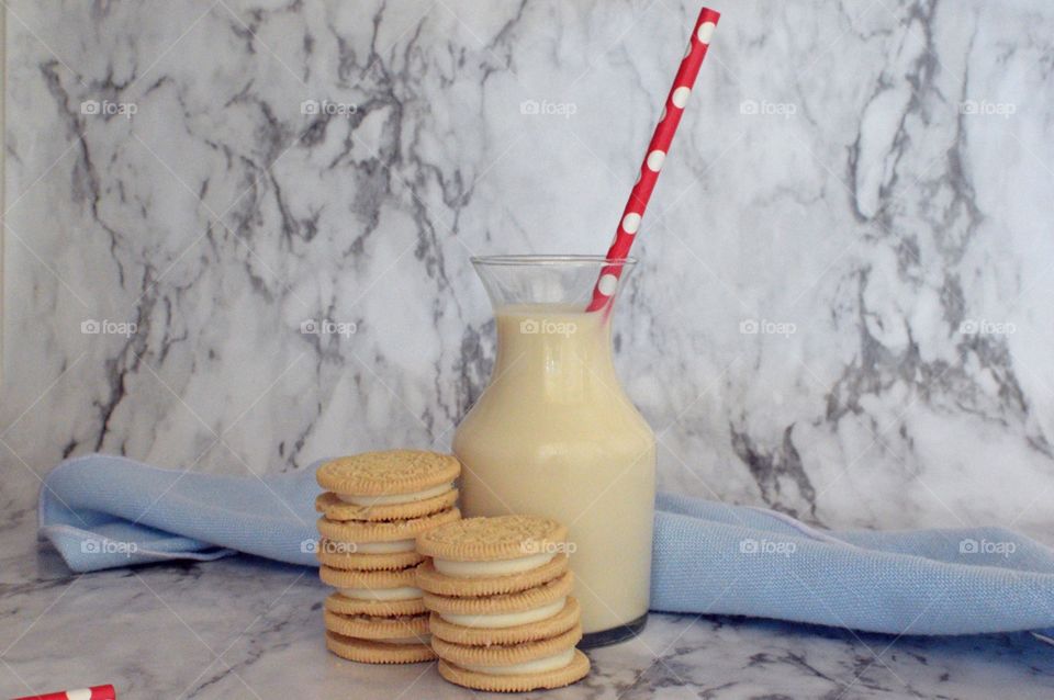 Oreo double stuff cookies stack next to a carafe of milk with a red and white straw on a marble backdrop