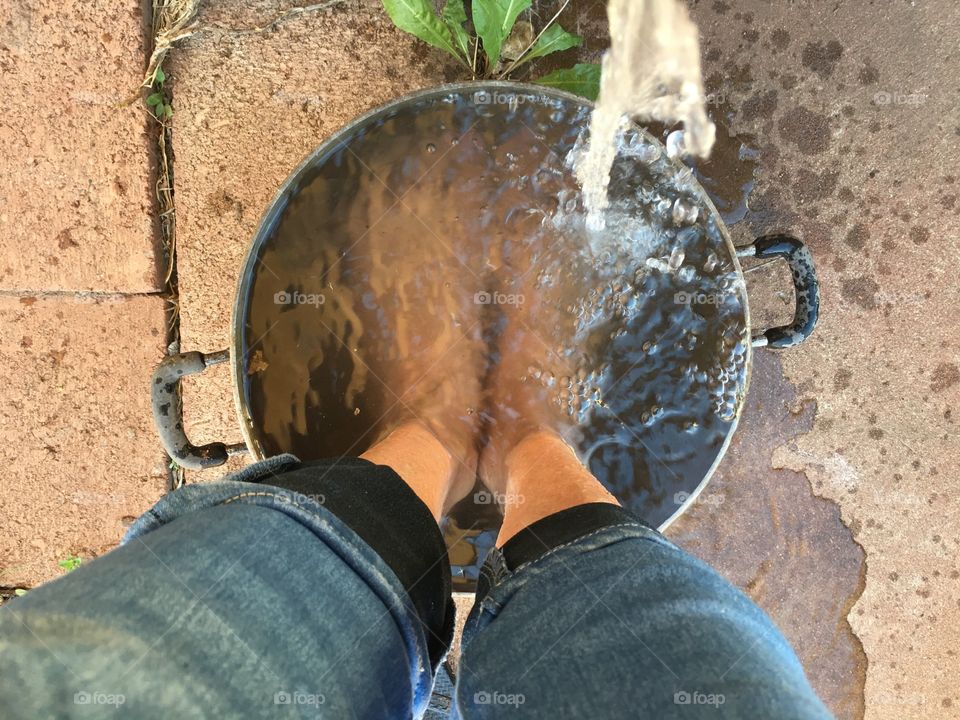 Water from outside tap outing over bare feet on metal bucket