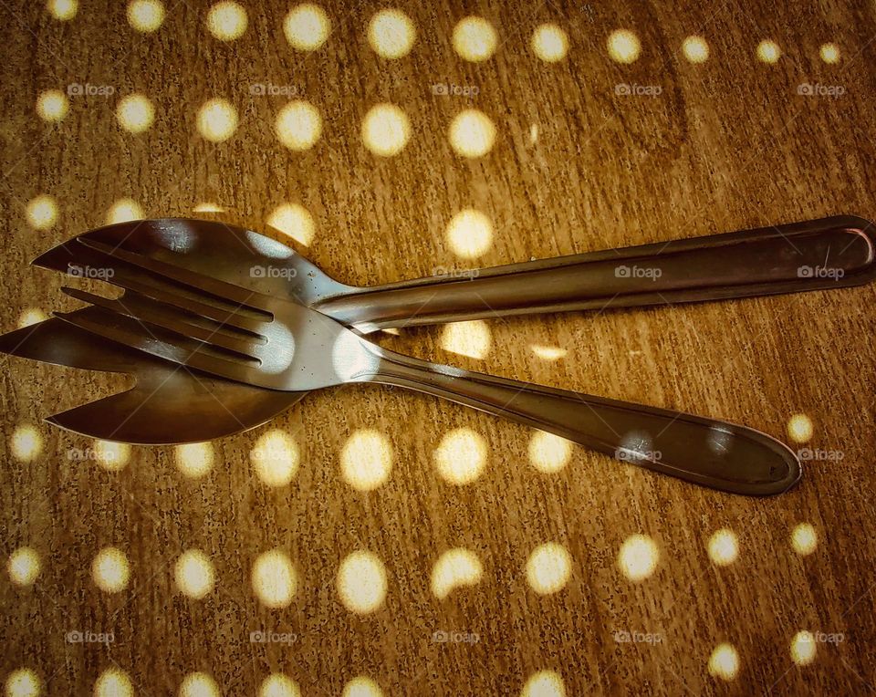 two forks of different shapes, on a flat wooden surface illuminated by small circles of sunlight