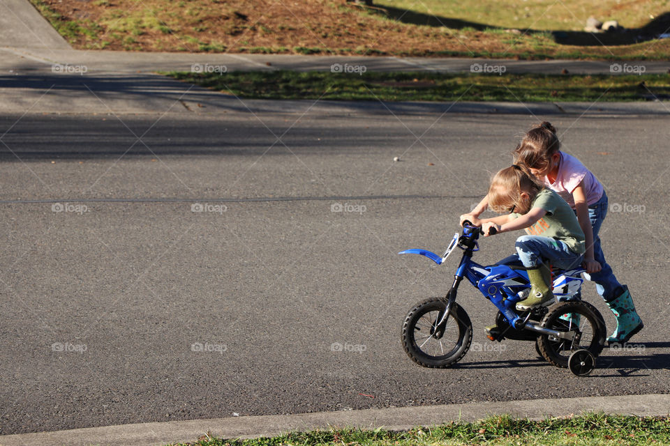 Sister teaches sibling how to ride a bike