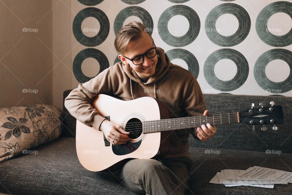 Young millennial man playing guitar learning online using music sheets 