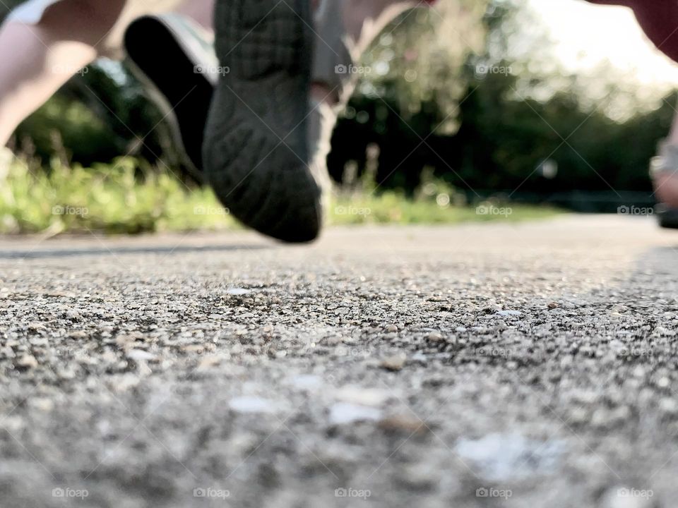 Running children macro shot focusing on the concrete ground by the grass and black sole under shoes in the action of their going. 