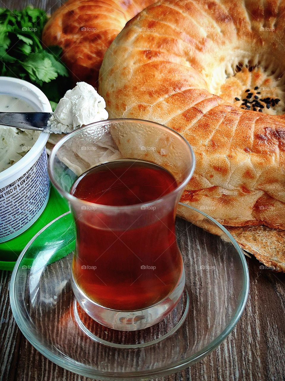 Food.  Breakfast.  Eastern food.  On a transparent saucer stands a glass of Armuda with black tea.  In the background is a jar of curd cheese and a knife with a white curd son.  Also in the background lies fresh pita bread.