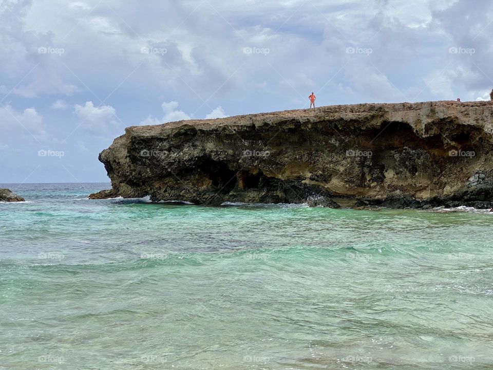 A person standing on top of a cliff overlooking green and blue water