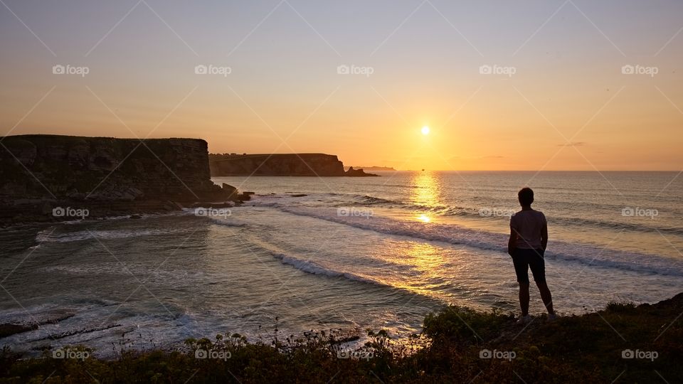 Woman contemplates the sunset at the edge of the cliff