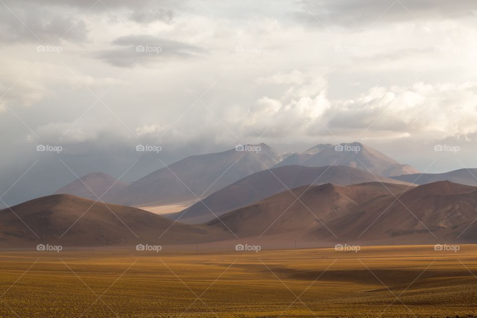 Desert scenery in Atacama. Mountains and valley in cloudy Atacama desert. Valley grass is yellow, mountains red