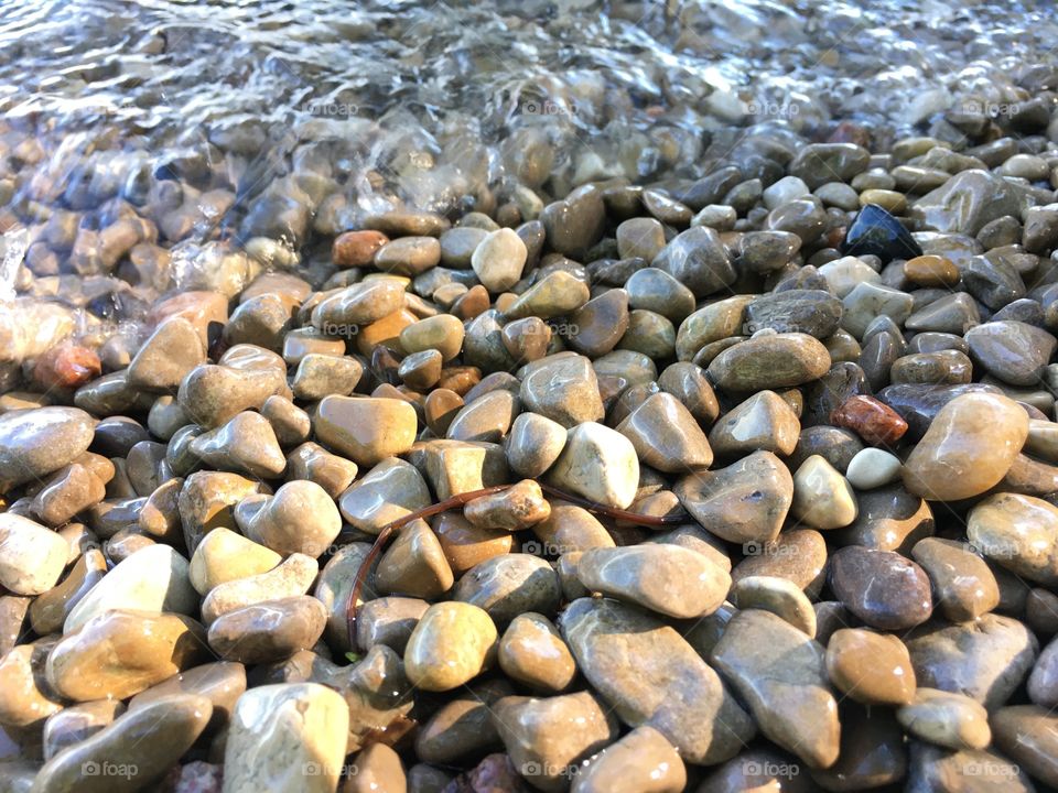 Smooth pebbles at waters edge with small waves washing over them closeup low angle view full frame nature and environment weathering or zen tranquil background 