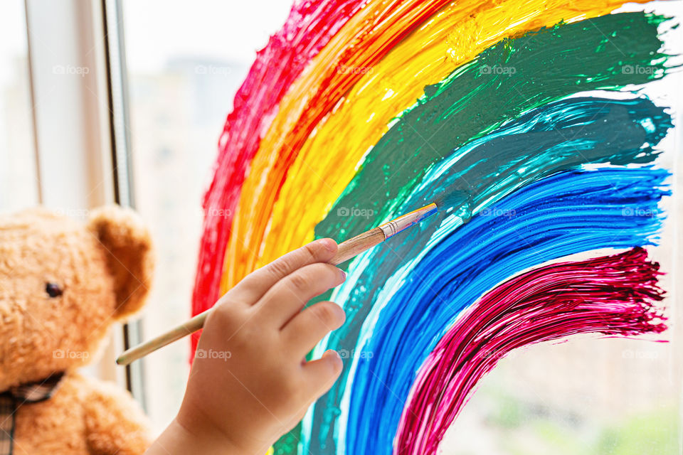 Kid painting rainbow on window 