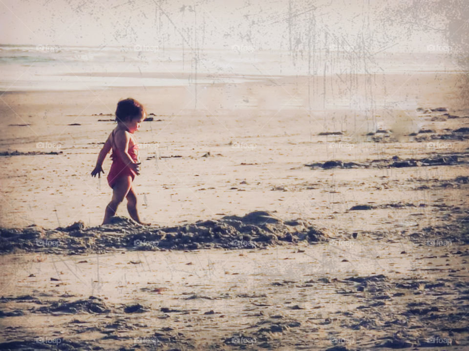 A little girl walks down the beach while playing in sand. vintage feel.
