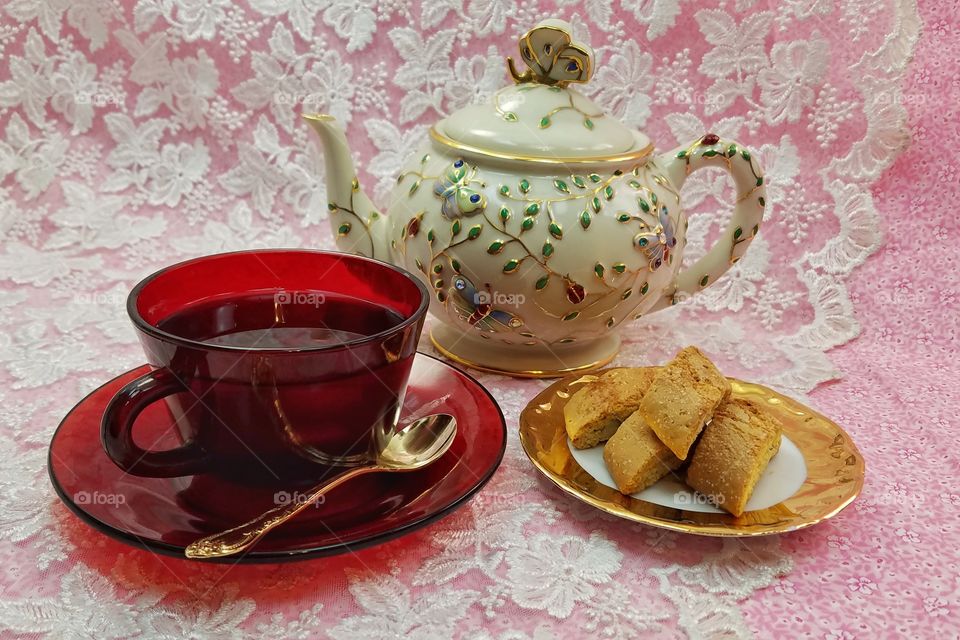 red hot cup of tea with beautiful teapot and biscotti served on a golden plate
