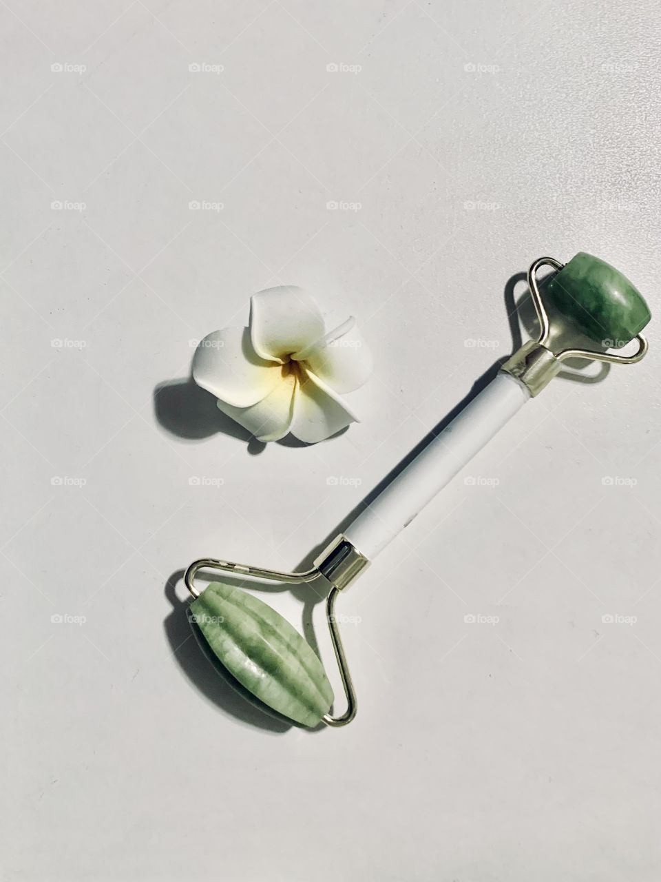 Jade facial roller and soft white flower displayed on a white background 