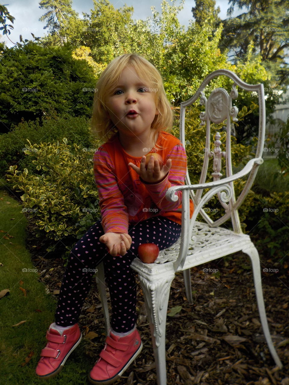Little girl sitting on chair holding apple