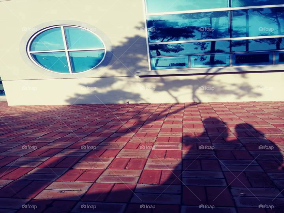 the shadow of a mother  sitting on the chair  while  her daughter standing beside her. the mother hugging the waist of her child.