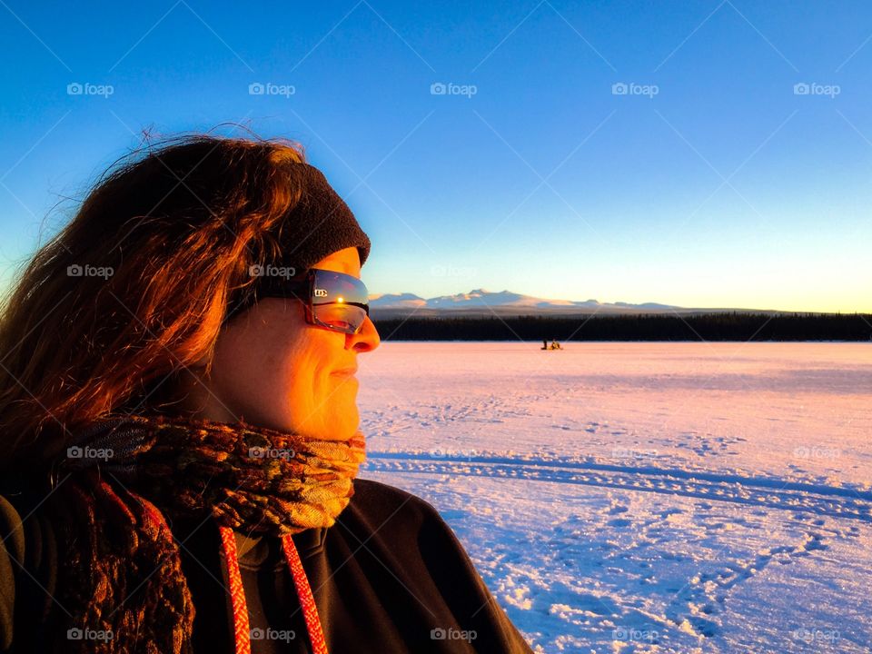Looking beyond the frozen lake as the sun sets on the horizon. Mountain backdrop and Mountain Msn on the snow machine. 