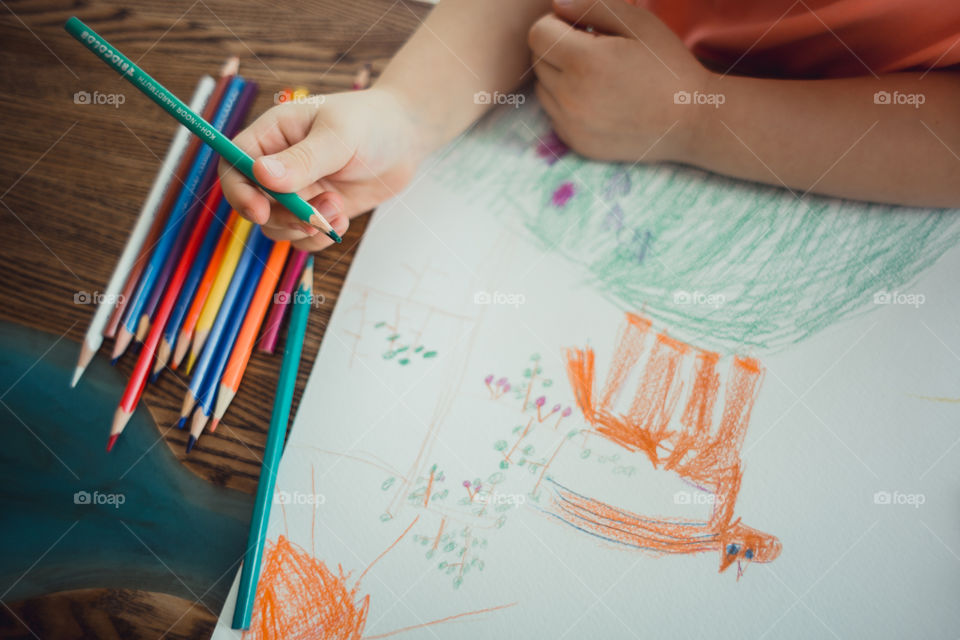 Little girl drawing with colorful pencils at wooden desk indoor