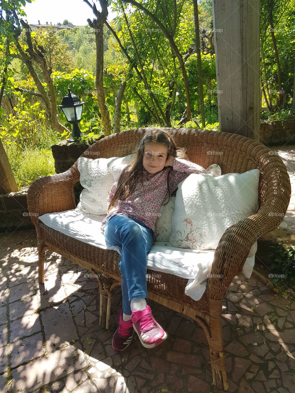 Girl sitting on a wicker sofa in the garden of a cottage in spring