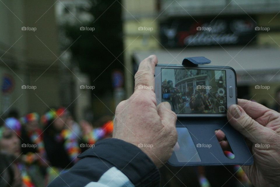 Old man hands taking a photo using a phone during carnival