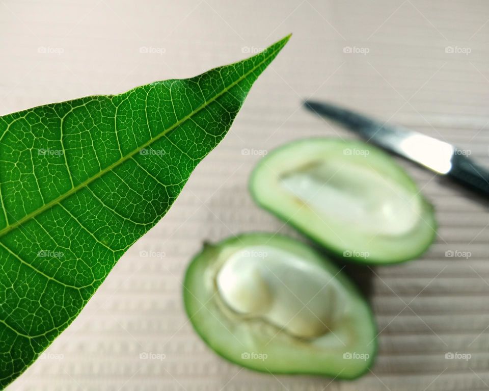 closeup of green leaf against slice of green mangoes and knife on pink background