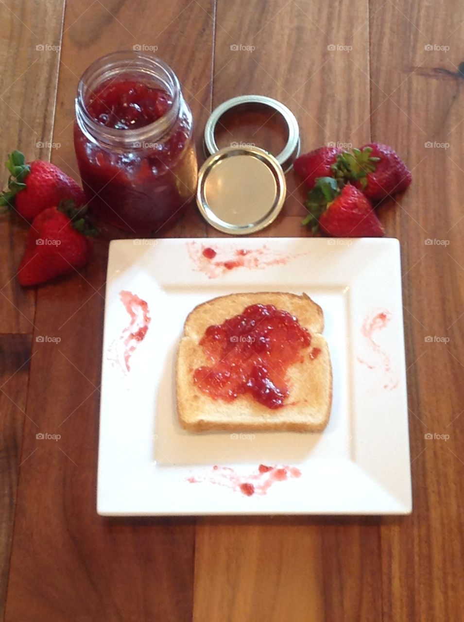 Homemade strawberry jam in a jar with a slice of toast.