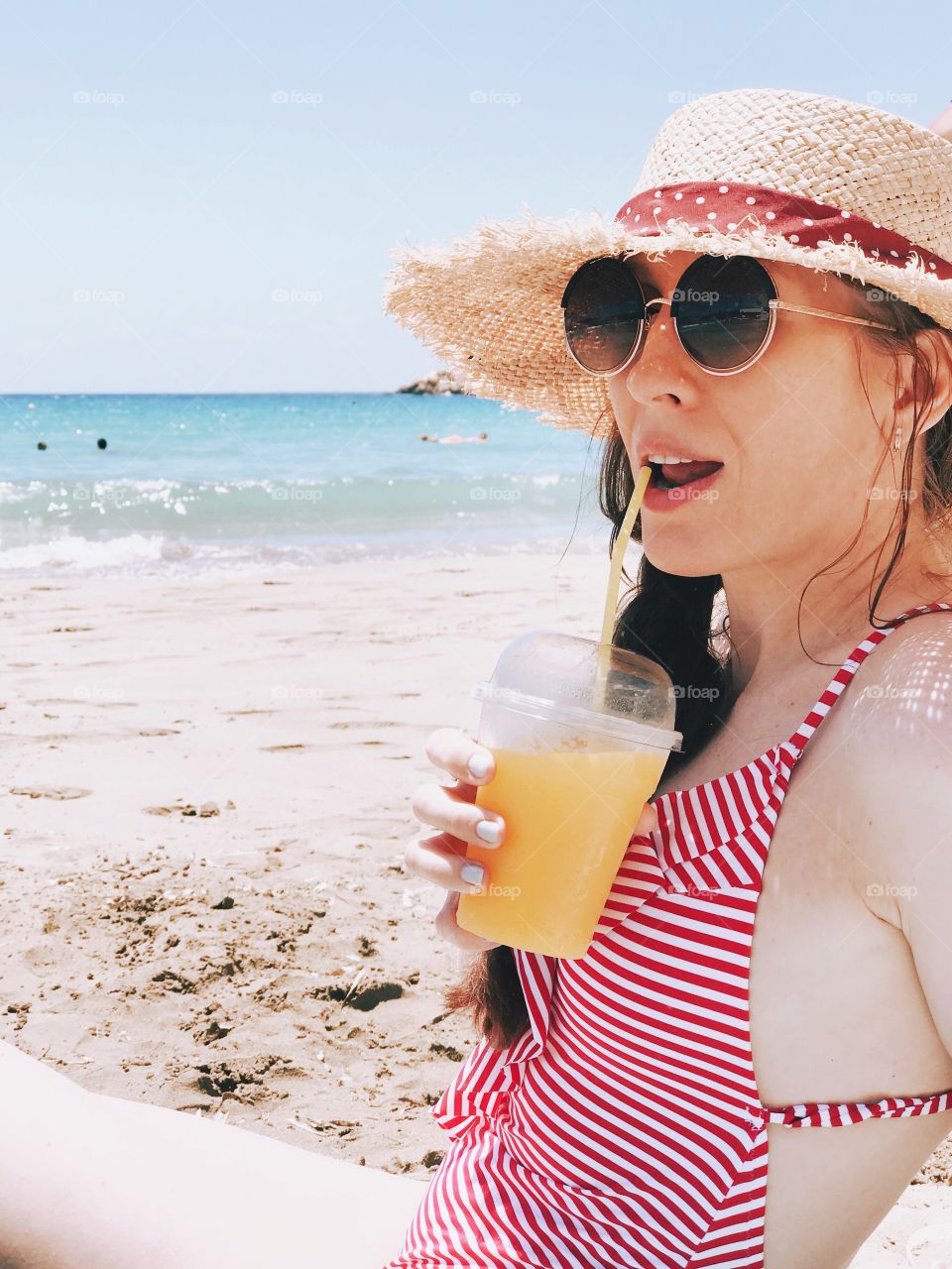 Girl in the straw hat drinking juice on the beach