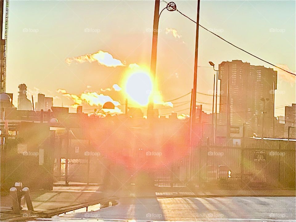 An intensely bright golden sun is about to set behind the horizon at Long Island City’s Newtown Creek in Queens, New York. 2021. Hypnotic Productions
