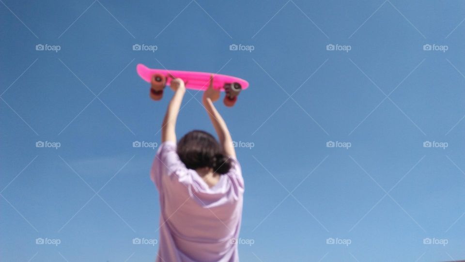 Young girl holding  pink skate board.