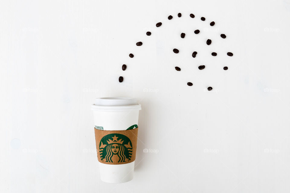 A Starbucks coffee cup laid out on a white table with coffee beans appearing to sprout out of the top