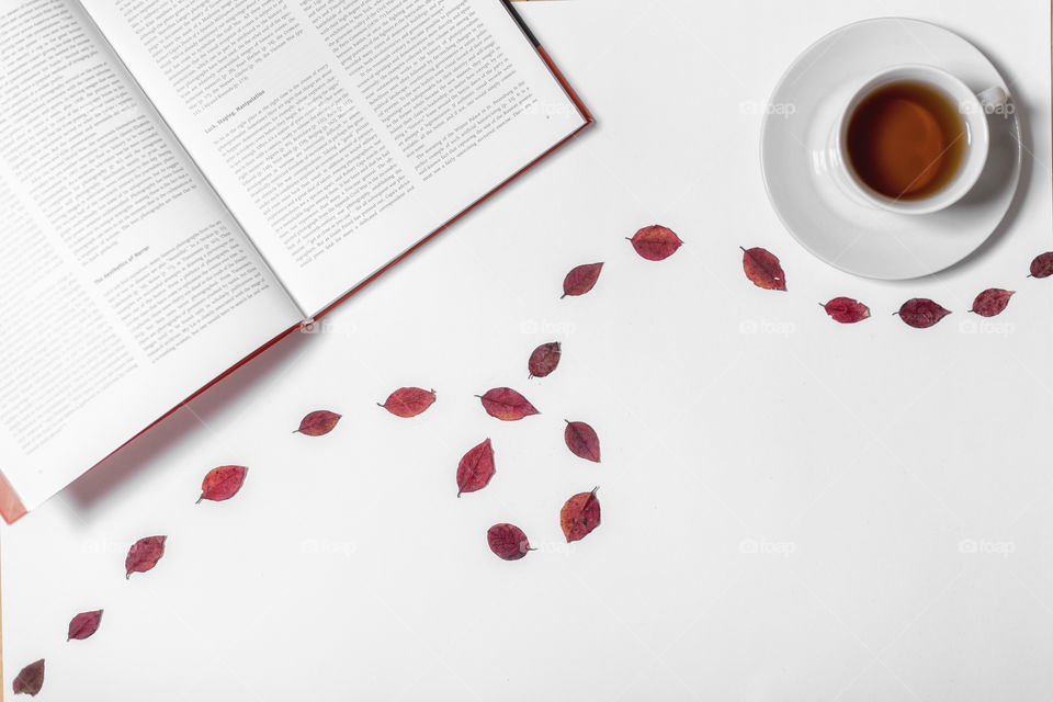 Flatlay opened book with leafs and a cup of tea beside 