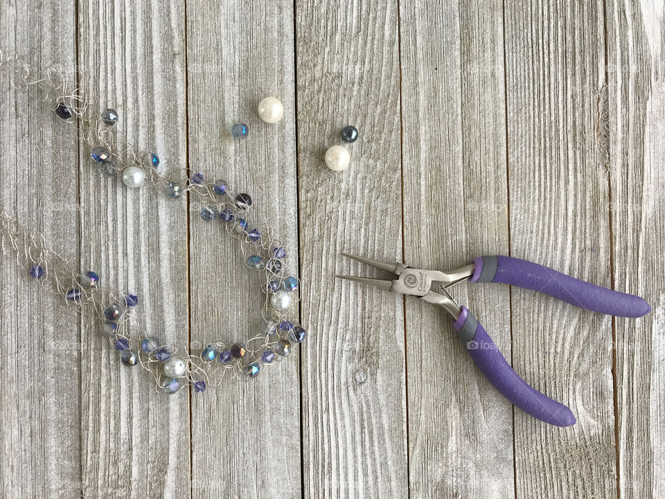 A crochet silver wire necklace with various shapes and colors of beads almost finished.