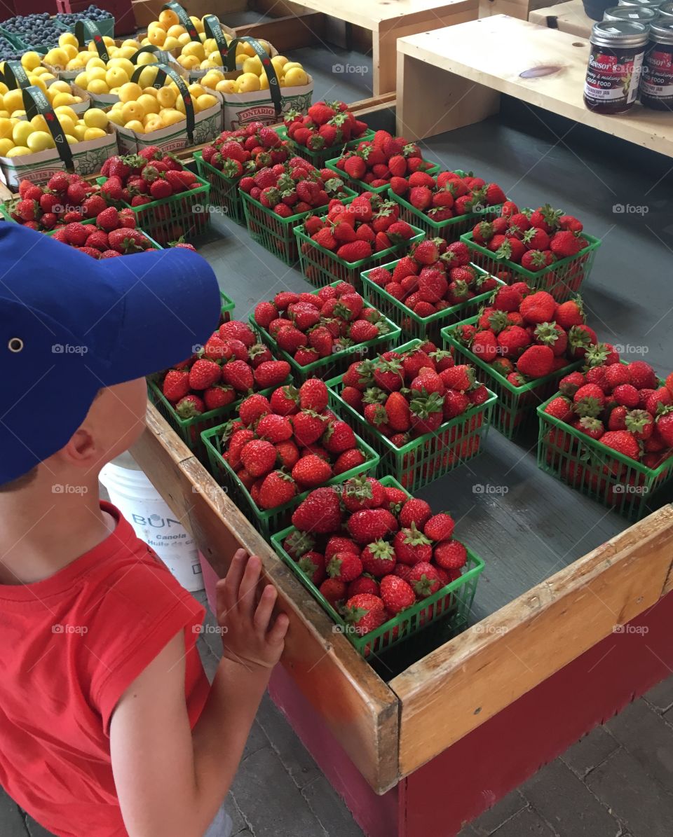 A young boy looking at baskets of strawberries. 