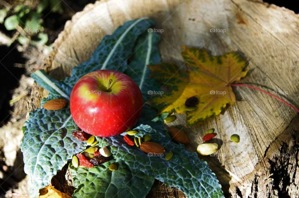 Conceptual healthy antioxidant and vitamin rich foods Red apple on Kale leaves with nuts and berries, almonds, goji berry, cranberry with maple leaf  in garden on natural wood 