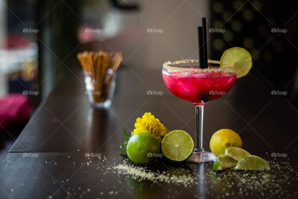 Red longdrink on ice with straw decorated with lemons on wooden table