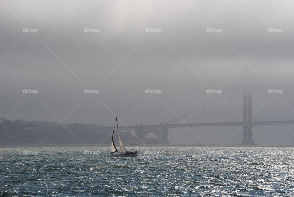 A group of sailors boating near the Golden Gate Bridge on foggy afternoon
