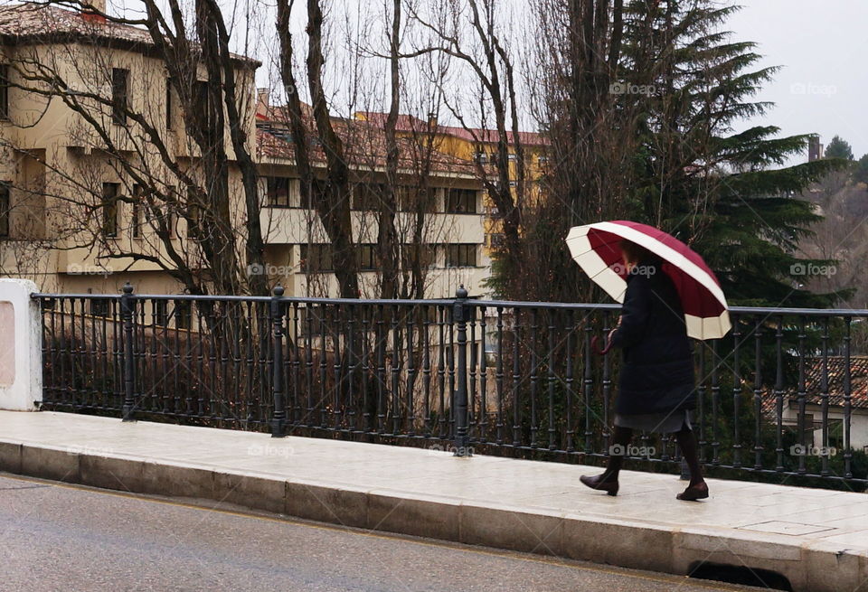 Woman walks by the bridge with red umbrella