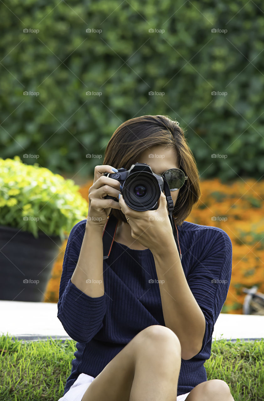 Hand woman holding the camera Taking pictures Background of trees and flowers