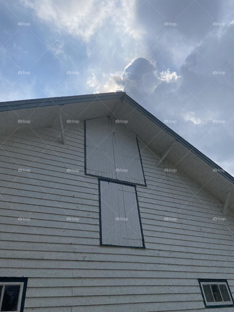 A partial view of the side and roof of a horse barn against the blue sky and clouds. This photo was taken in Thompson Park in Lincroft, NJ. It is one of several farm buildings at the park that were once used for breeding Thoroughbred racehorses. 