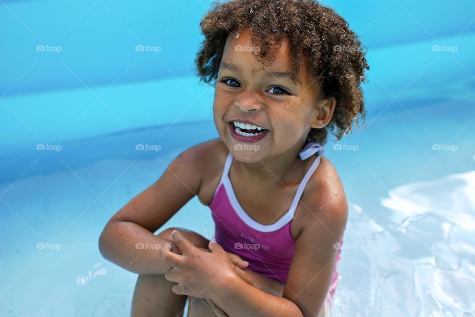 Girl of mixed race enjoying the refreshment of water in a swimming pool on a hot summer day, together with her little sister (family, fun, summer, water, blue, swimming suit, splash, hot, enjoy, play, outdoors)
