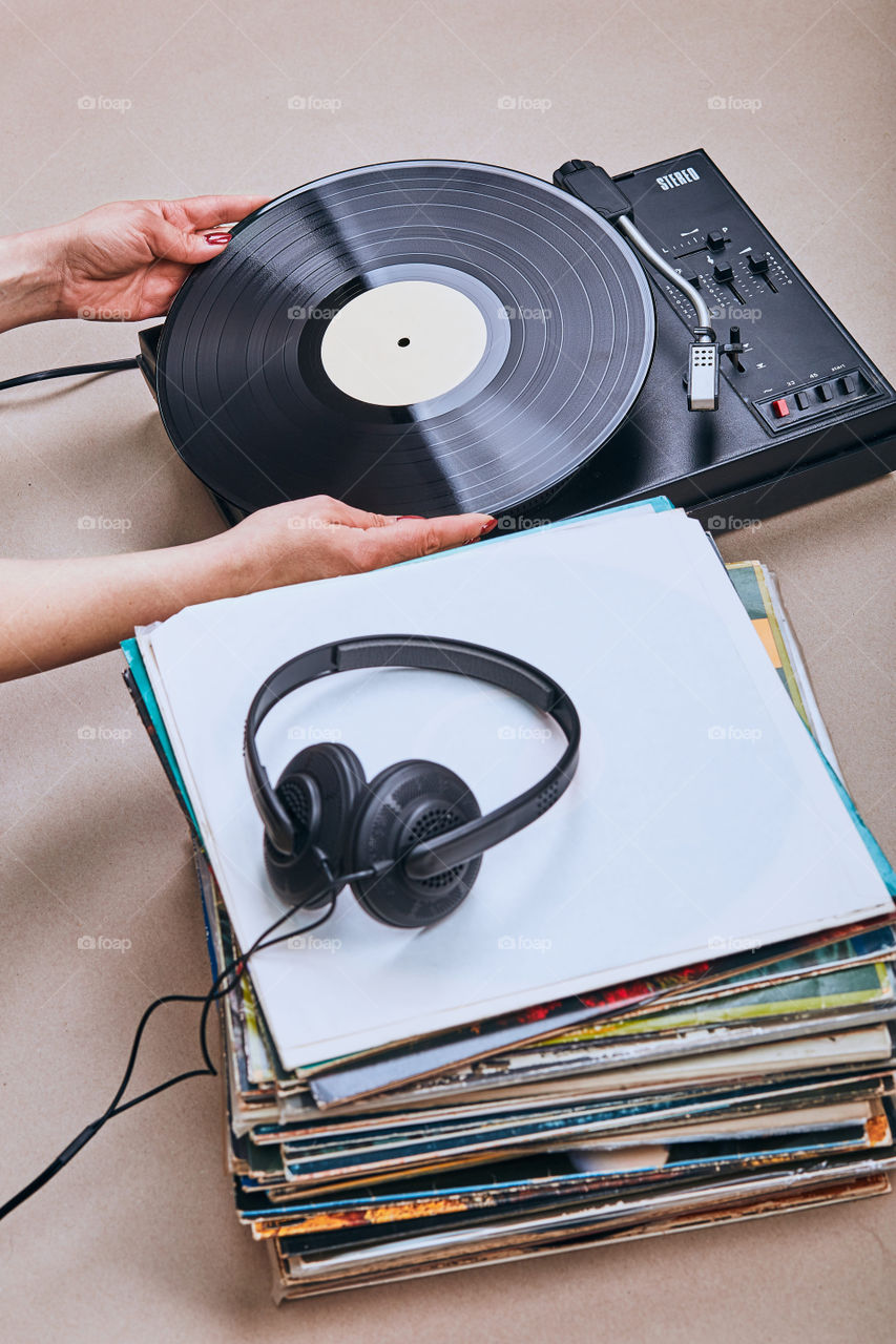 Stack of many black vinyl records, turntable vinyl player and headphones put on the stack. Classic stereo set. Candid people, real moments, authentic situations