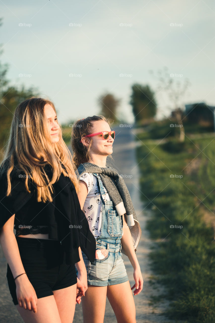 Teenage smiling happy girls having fun walking outdoors, hanging, spending time together on summer day. Real people, authentic situations