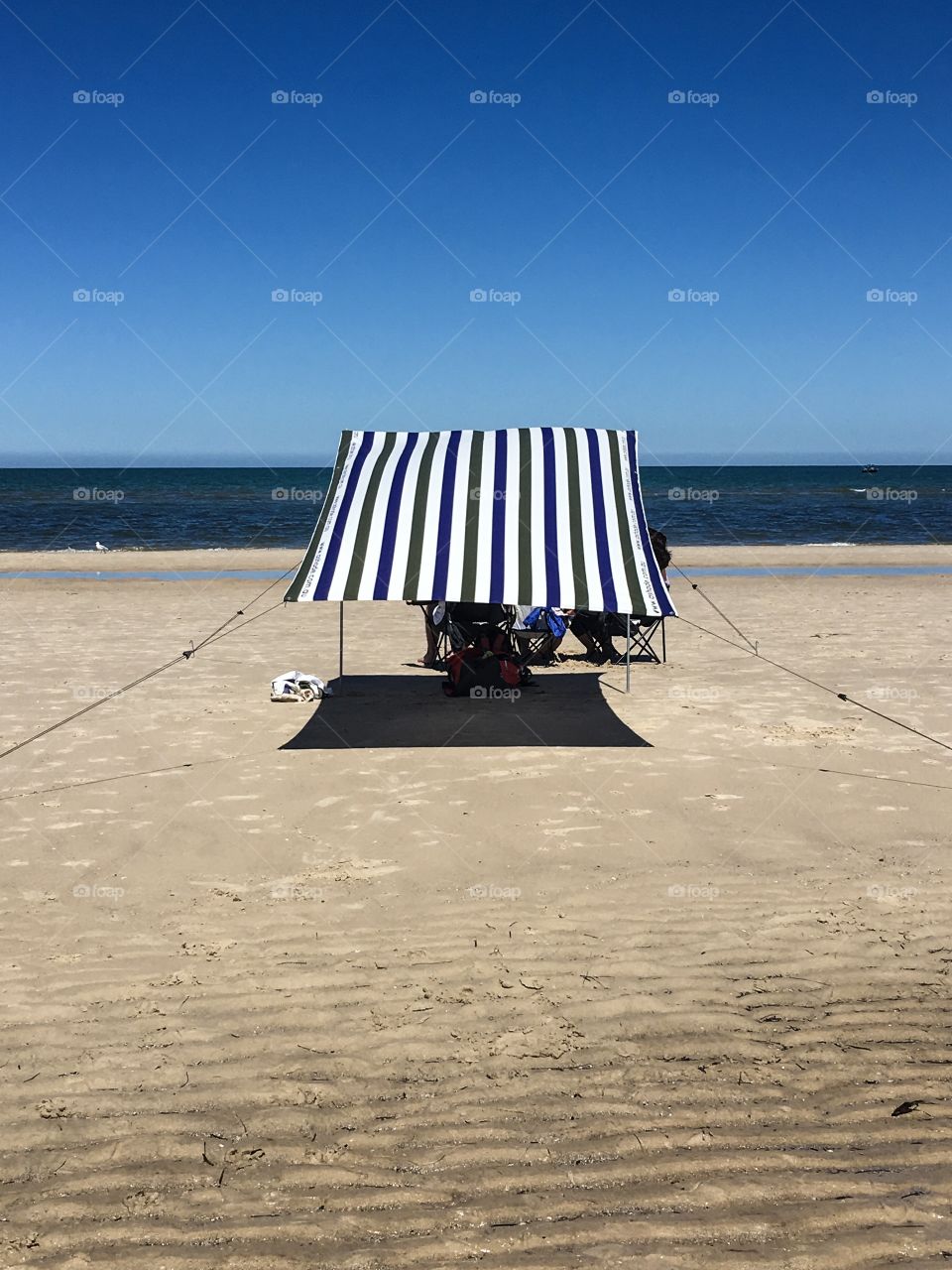 Beach chair with dark blue striped sunshade  on tropical remote beach facing horizon on clear blue day. 