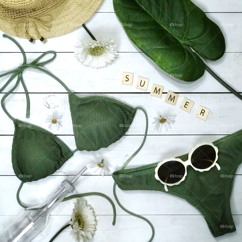 Summertime flat lay with green swimsuit, water bottle, sun hat, sunglasses, and flowers ☀️