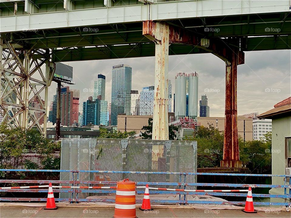 This is a the LIC and „Manhattan“ skyline seen through the metal support structure of the „Brooklyn Queens Expressway“ running parallel to „Borden Ave“ and the „Borden Avenue Bridge“ over „Dutch Kills“ in LIC, Queens. 2023. Hypnotic Productions