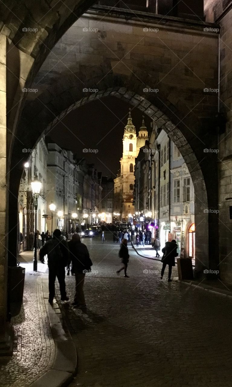 Beauty of the night - A photo of an illuminated church steeple taken through the arch’s of Charles Bridge in Prague 