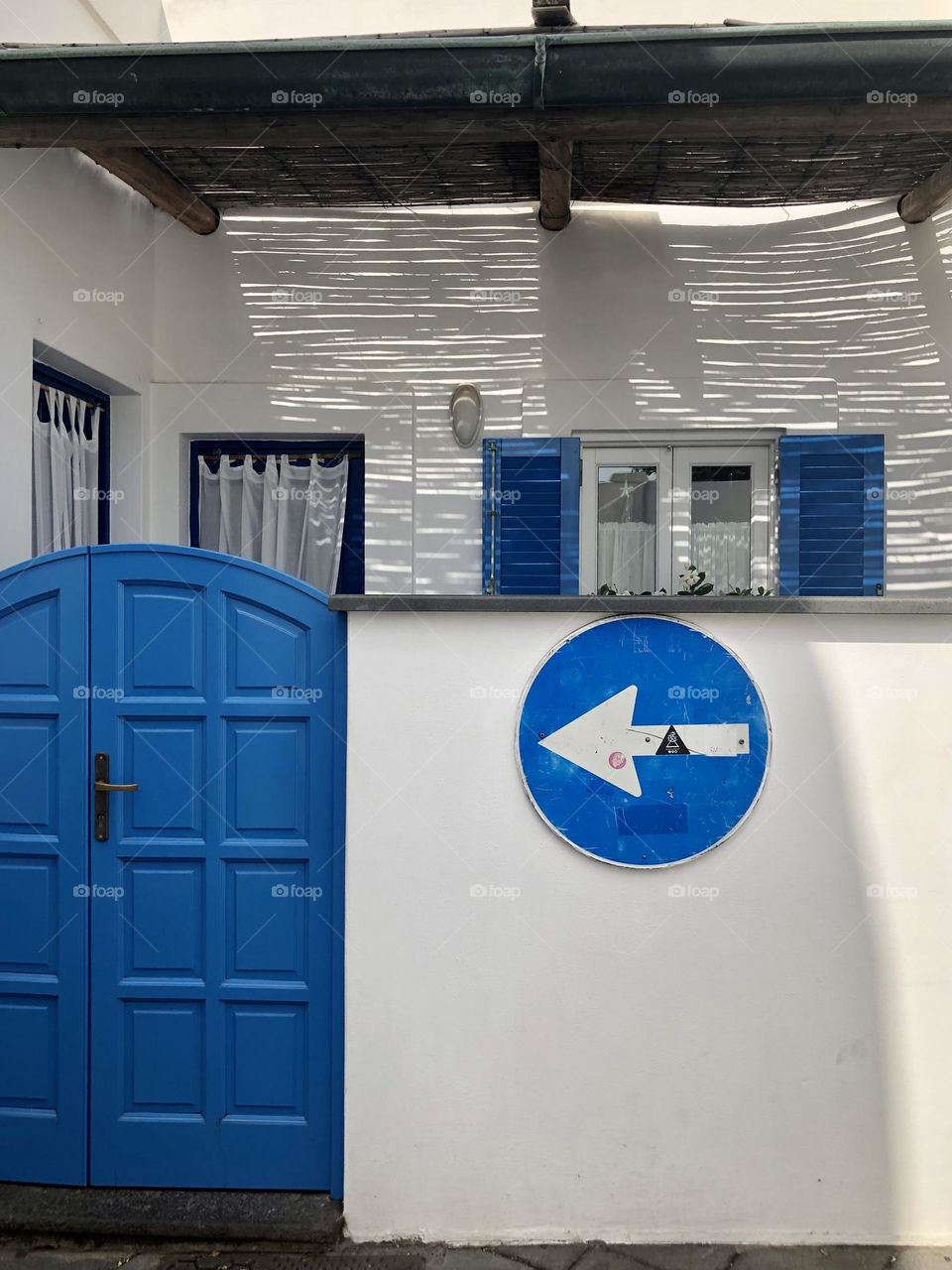 Entrance patio of a house with blue doors and windows, and blue road sign on white washed wall, Panarea island, Italy