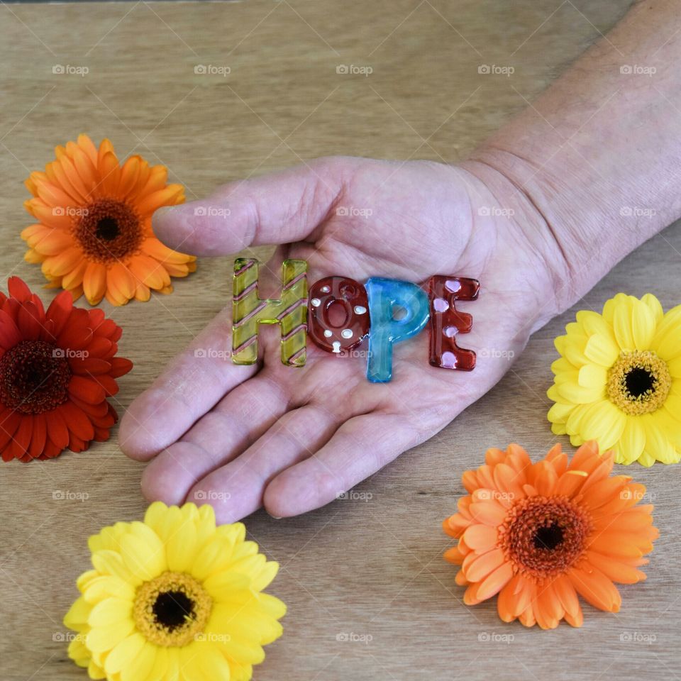 Hand holding art glass spelling hope surrounded by flowers