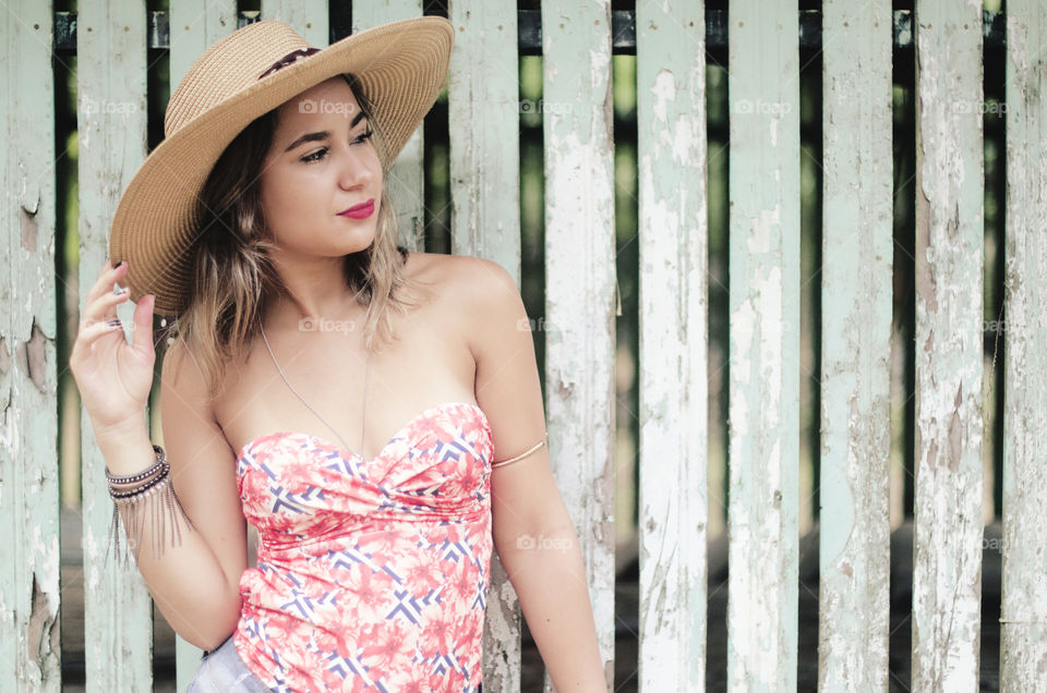 Pretty woman leaning on wooden fence wearing hat