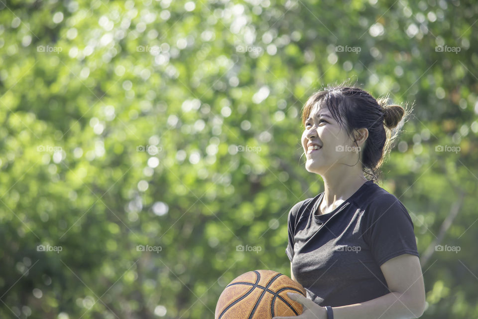 Basketball in hand Asian woman Background blur tree in park.