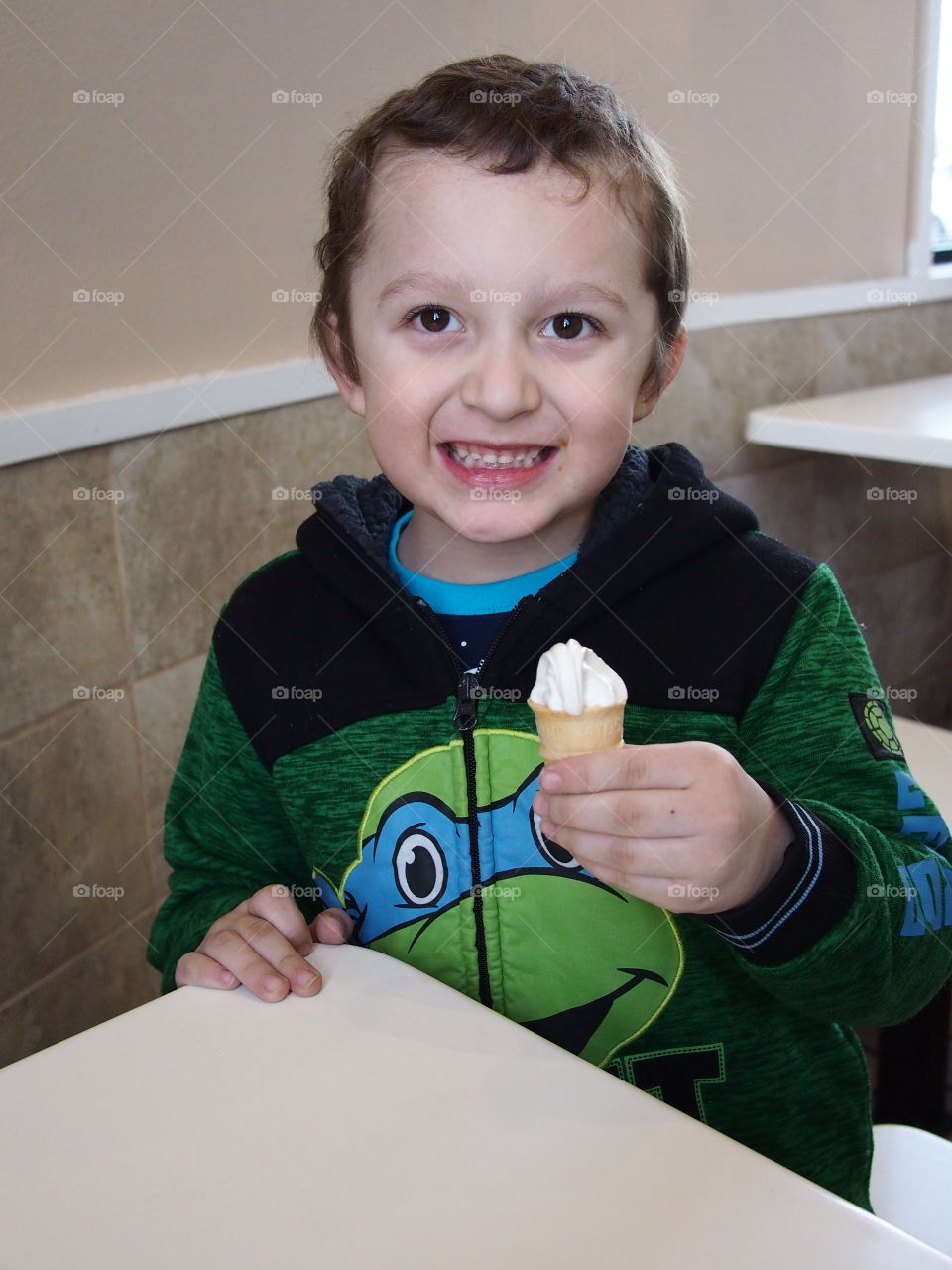 A little boy really enjoys his small vanilla cone that really hits the spot. 