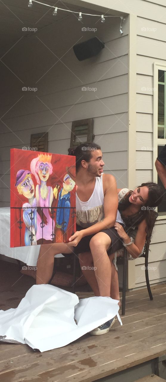 Smiling couple sitting on chair holding painting
