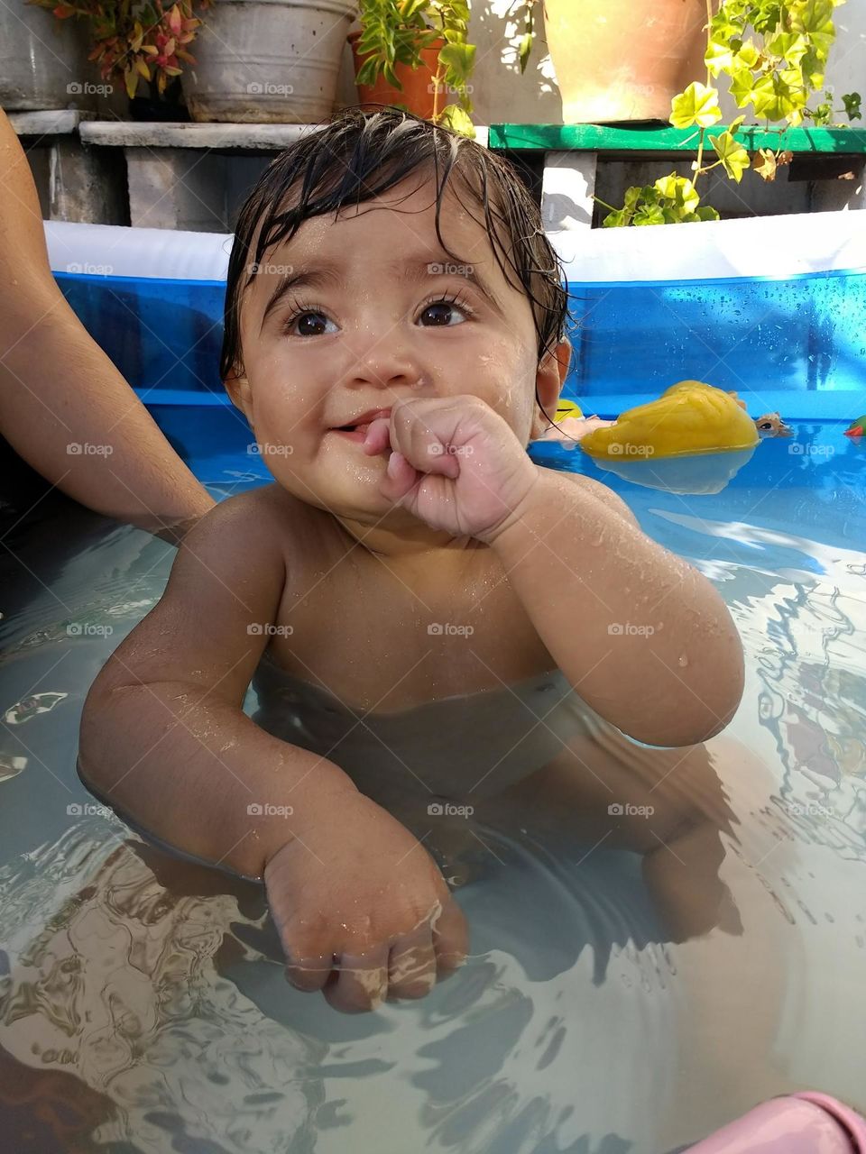 baby sitting in the pool looking up and sucking his hand
